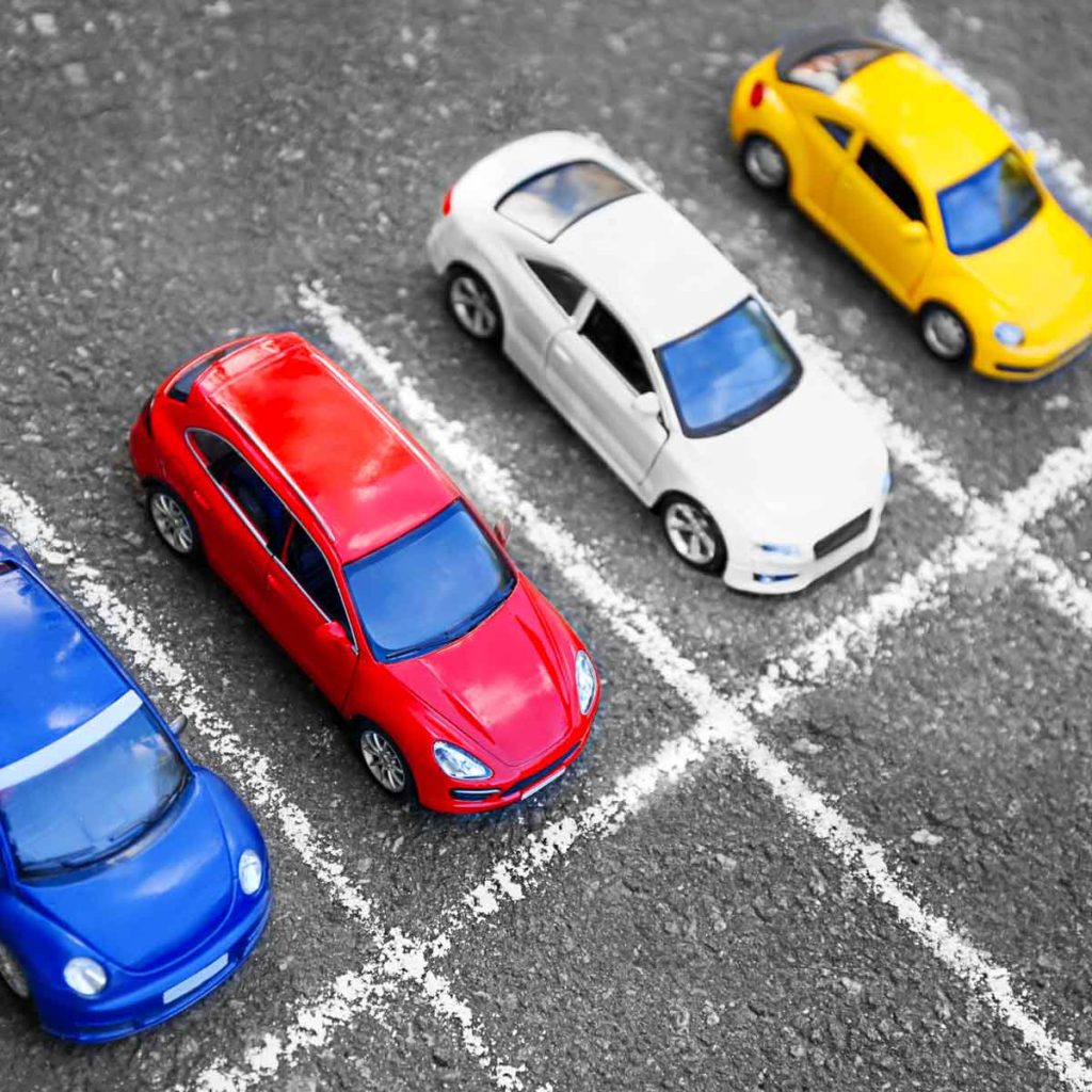 Toy cars in blue, red, white and yellow lined up behind chalk lines as if starting a race - but which car colour is best when you're buying your vehicle?
