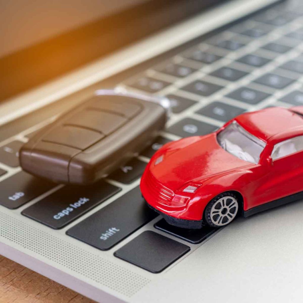 Model of a small red car next to a car key on the keys of a laptop - tips for buying from car manufacturer websites in the UK