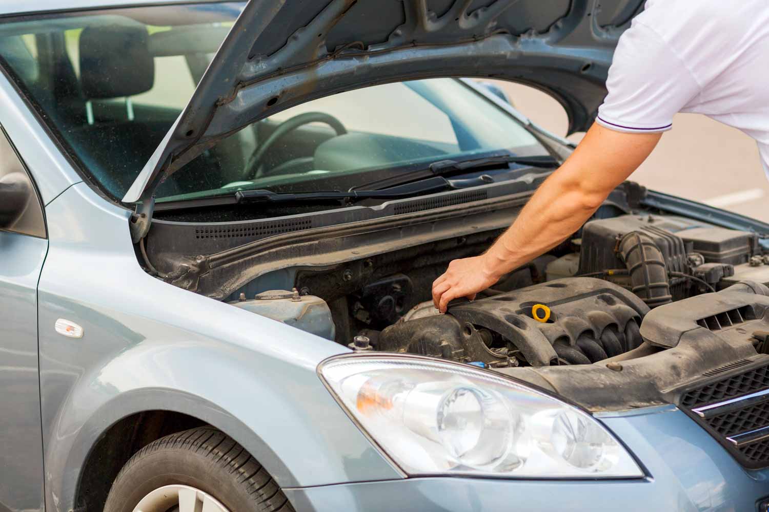 Man's arms stretched inside the bonnet of a silver car, partially seen - checking under the bonnet is one essential step in our guide to viewing a used car