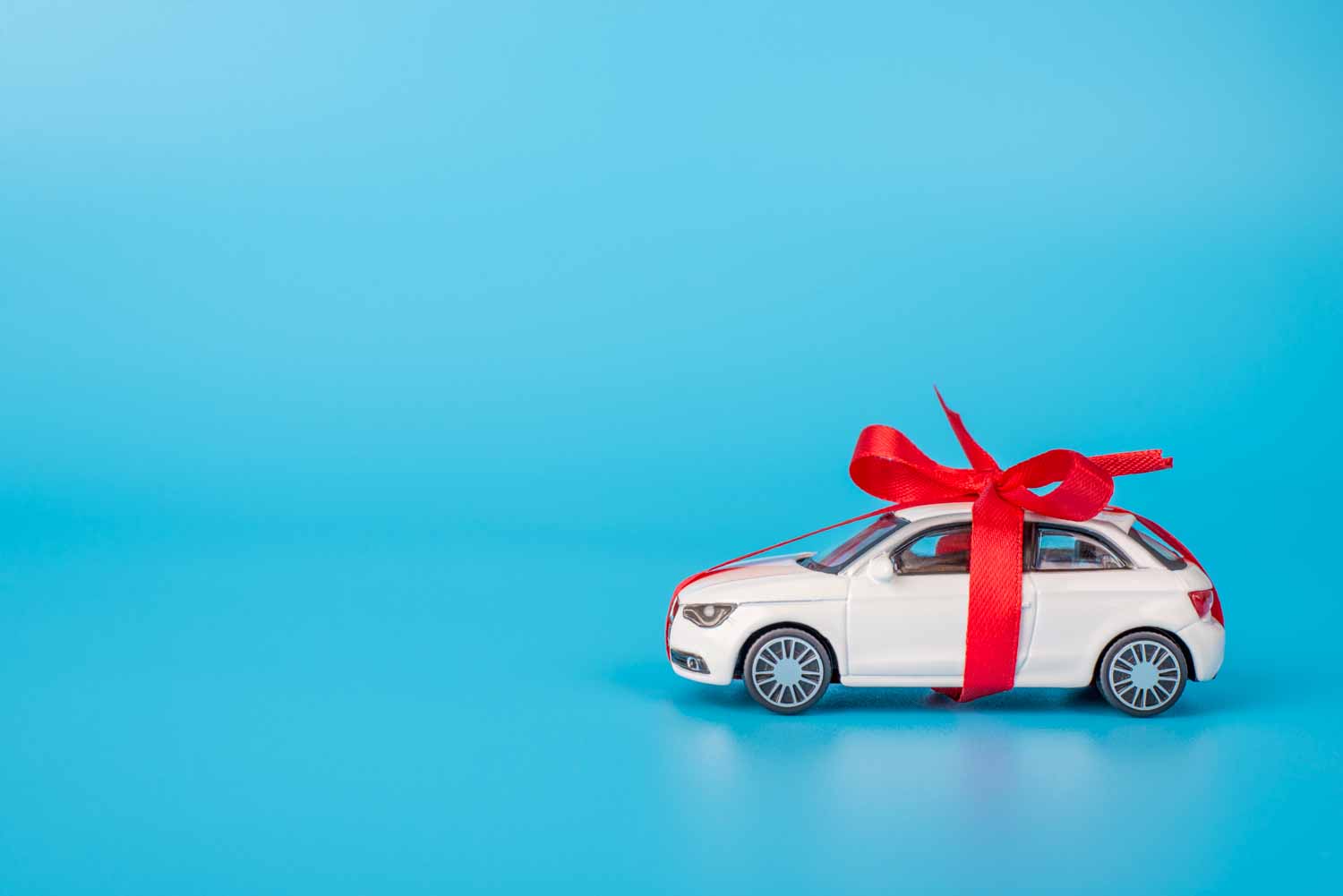 Small white car gift wrapped with red ribbon in a bow against a blue background - a tempting appearance isn't everything, and why a car data check is essential