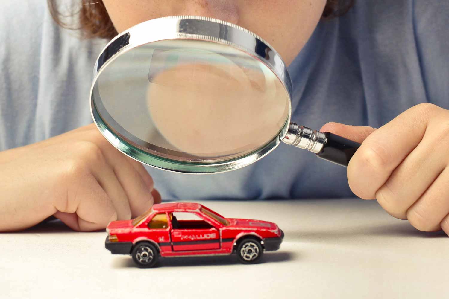 Hands holding a magnifycing glass, looking at a small red model car - our ultimate guide to viewing a used car